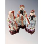 Three Chinese porcelain figures of deity on carved wooden stands,