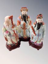 Three Chinese porcelain figures of deity on carved wooden stands,