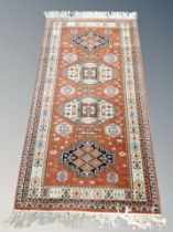A Caucasian fringed rug on coral ground 195 cm x 89 cm