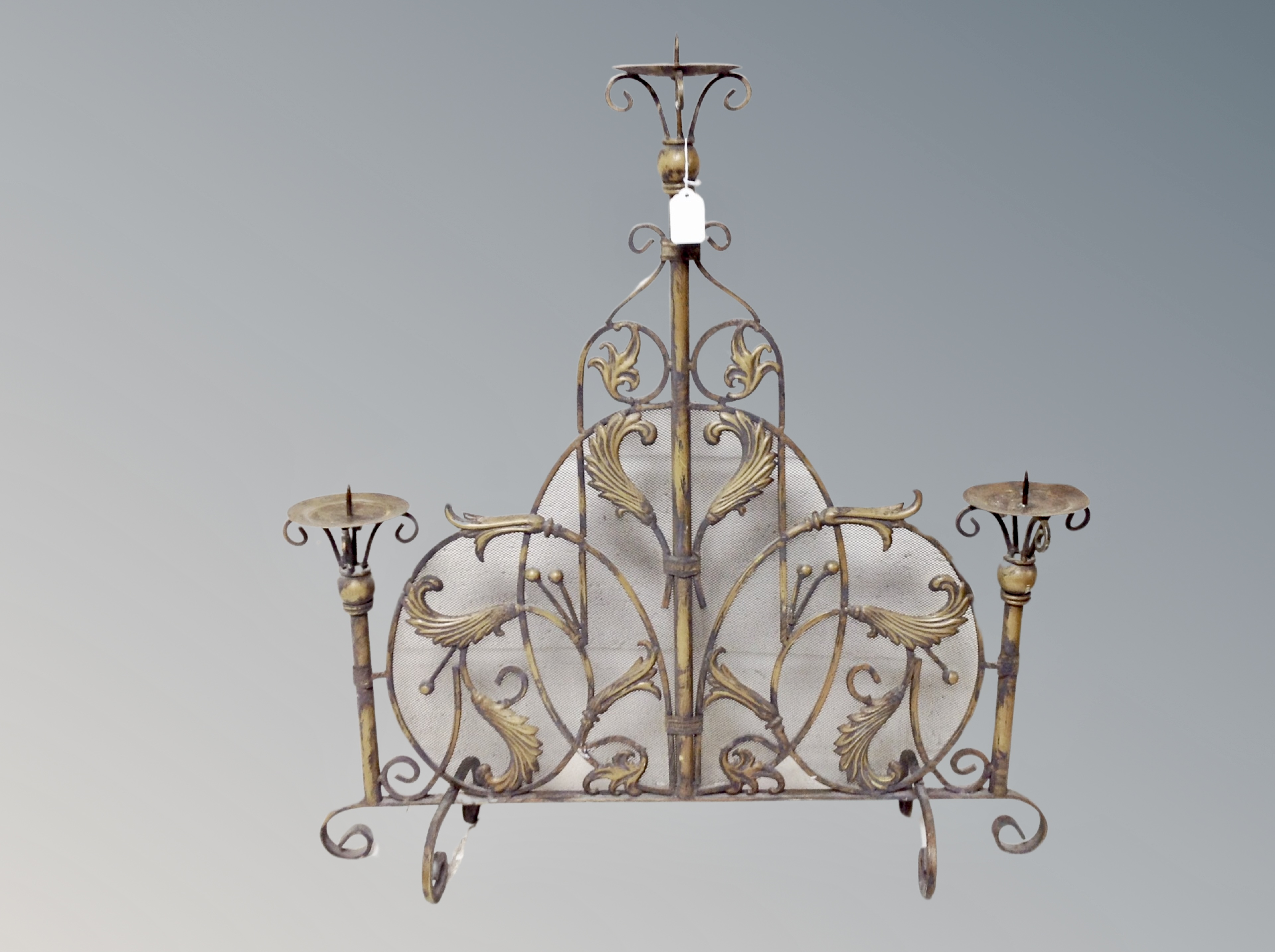 An ornate cast metal fire guard with three pricket candlesticks,