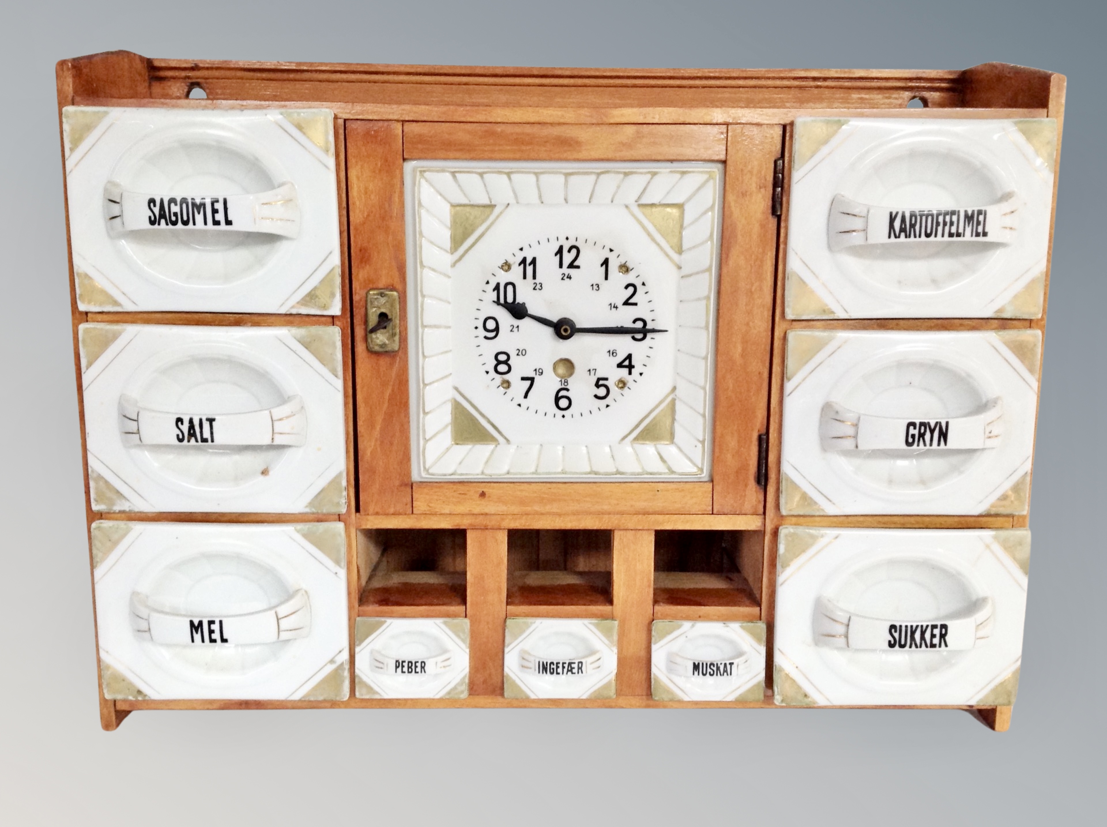 A Danish kitchen wall mounted spice cabinet with central battery clock and porcelain drawers,