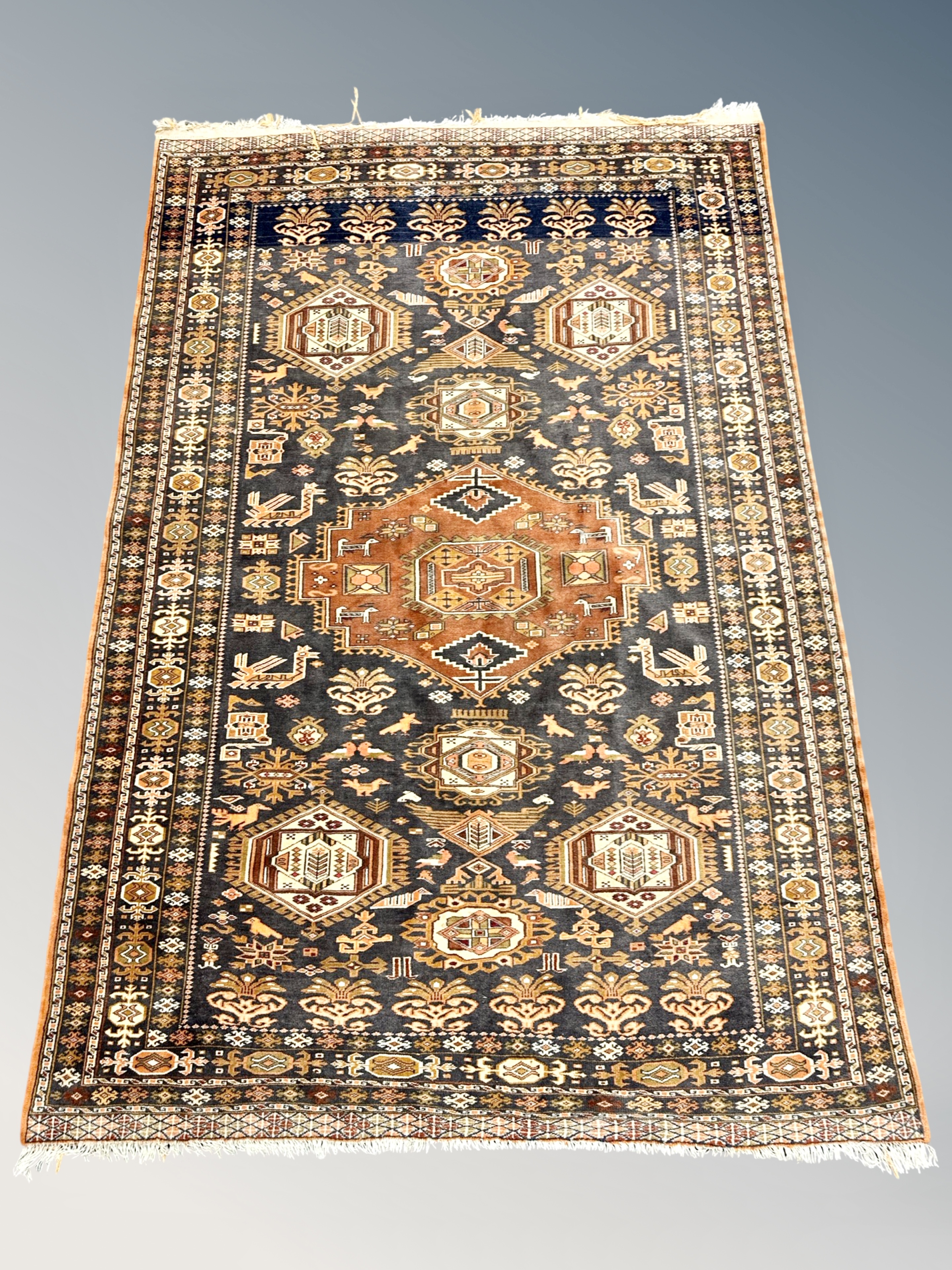 A Caucasian rug with stylised birds against a black field of hooked medallions and flowers,