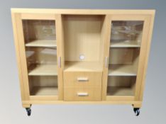 A contemporary double door glazed bookcase fitted with two central drawers on castors