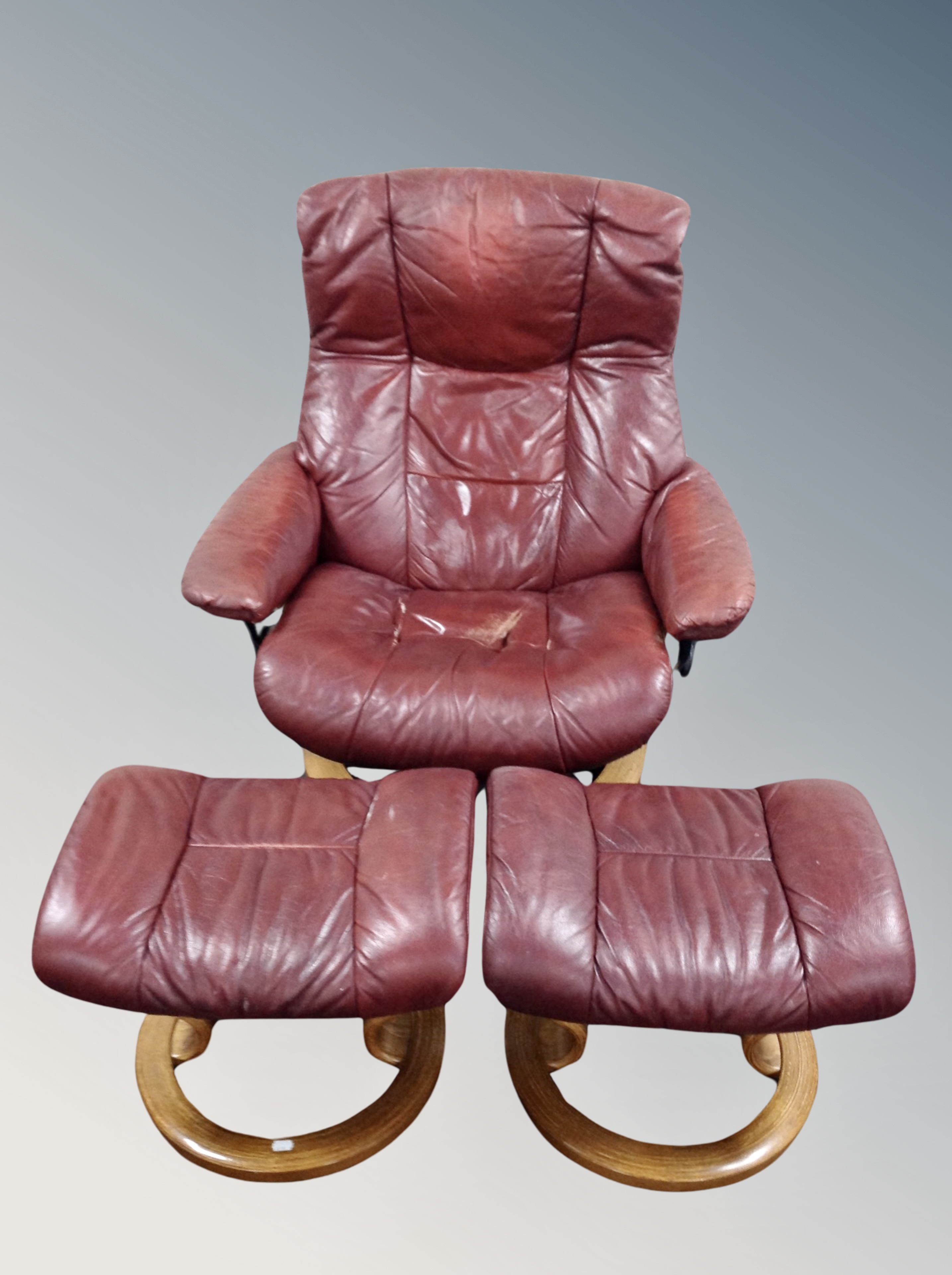 A Stressless swivel reclining armchair together with two stools in Burgundy leather