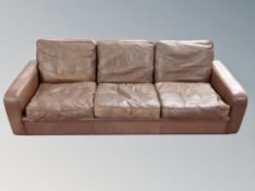 A Danish three piece lounge suite in brown leather comprising of three seater and pair of armchairs