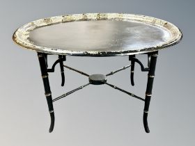 A Regency style papier mache mother of pearl inlaid and gilt oval tray on bamboo effect table with