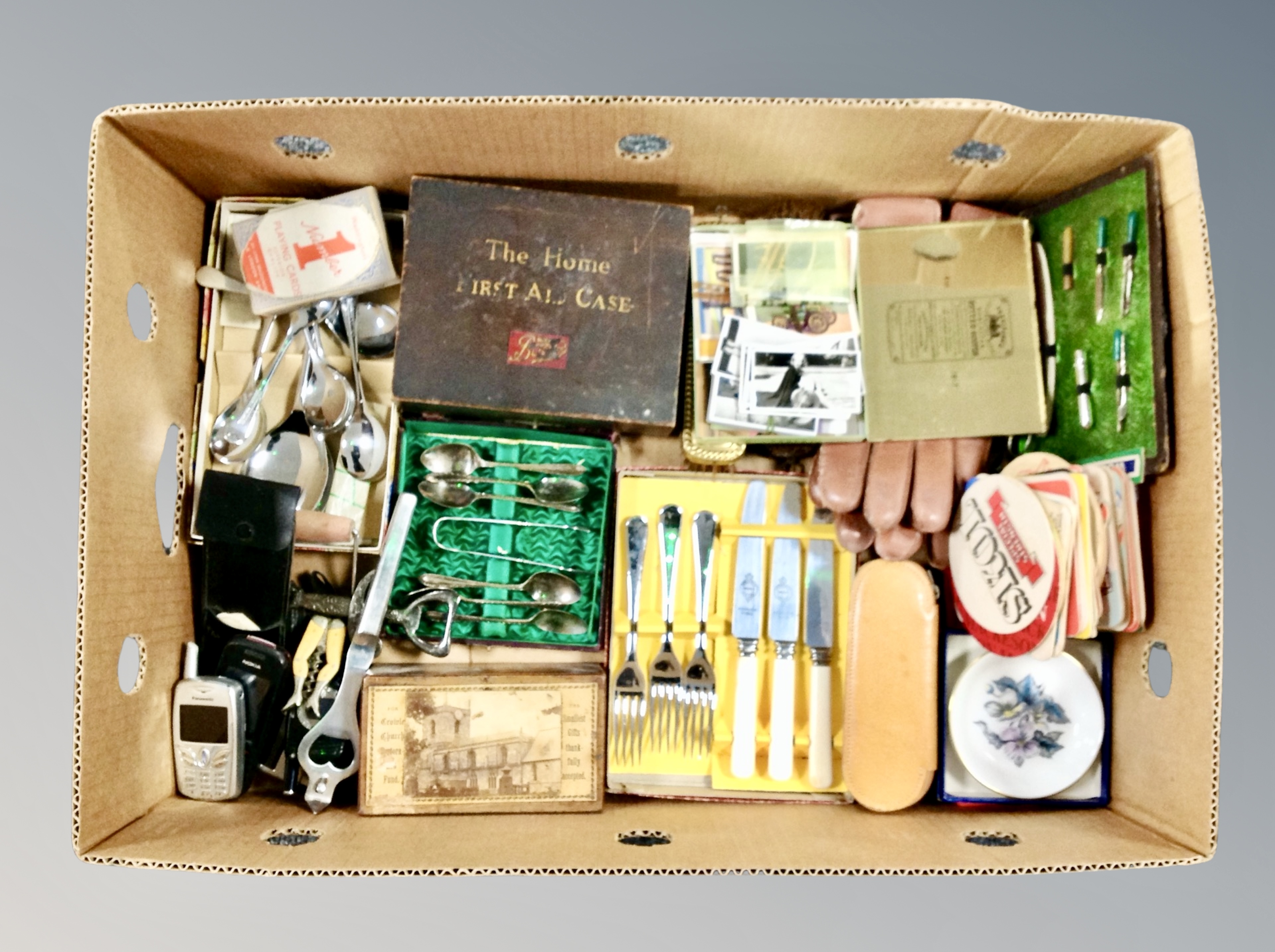A box of cutlery sets, vintage first aid box, boxed coasters, novelty corkscrew,