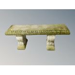 A weathered concrete garden bench on classical style supports,