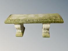 A weathered concrete garden bench on classical style supports,