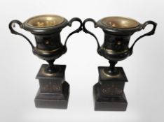 A pair of patinated metal urns on marble plinths,