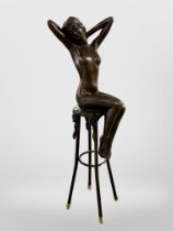 A bronze figure of a nude female seated on a stool,