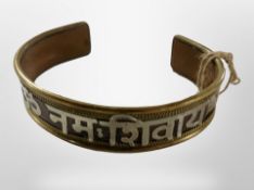 A decorative eastern copper, brass and white metal bangle with overlaid calligraphy,
