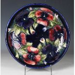A Moorcroft Pottery circular dish, 1920s, decorated with the Pansy pattern against a blue ground,
