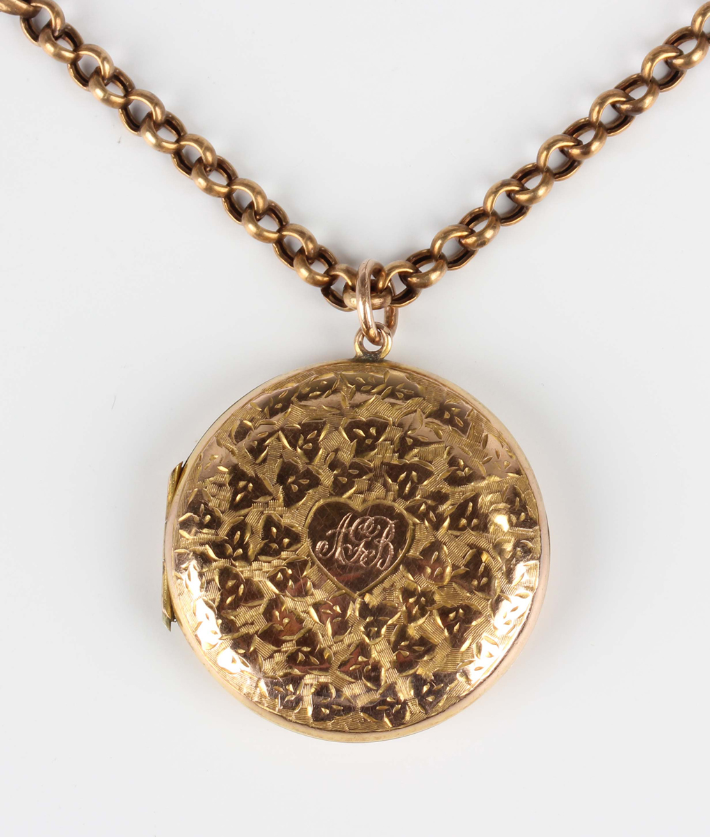 A gold back and front circular pendant locket with foliate engraved decoration, the front monogram