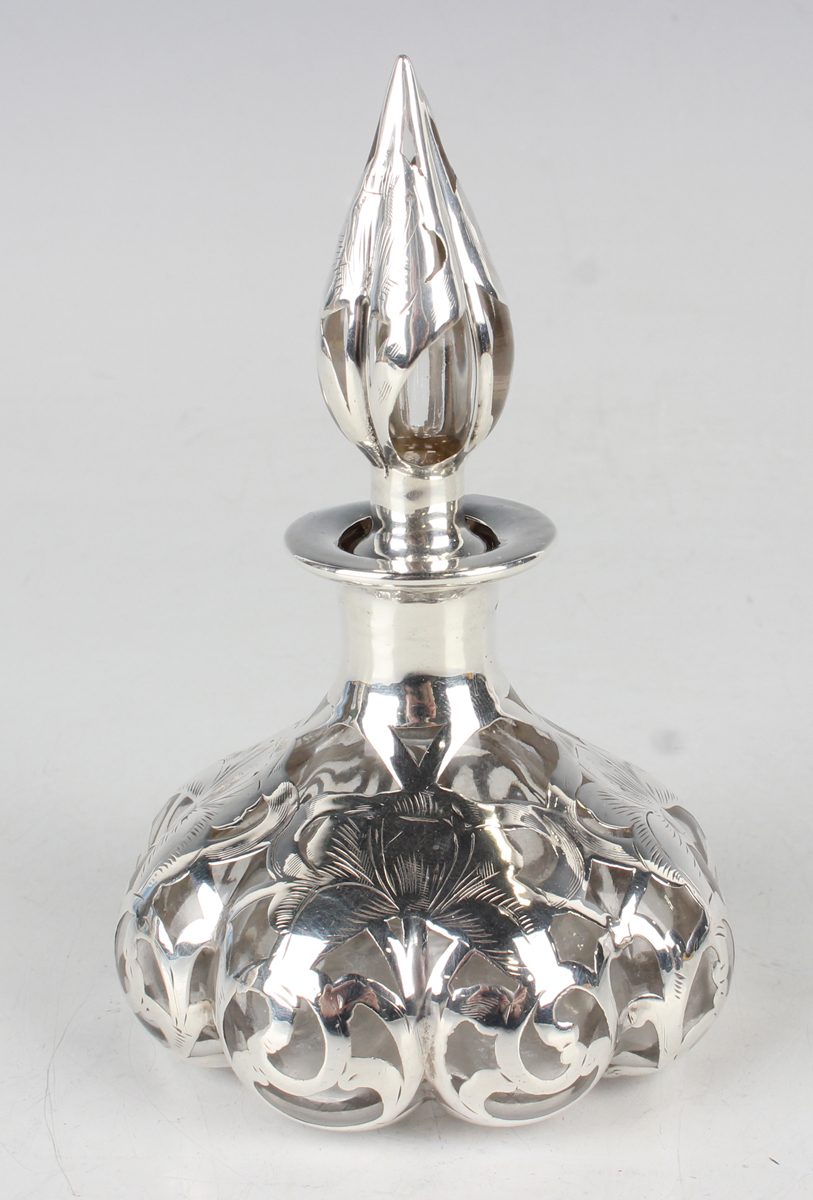 An early 20th century silver overlaid clear glass scent bottle and stopper, the lobed low-bellied