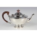 A George V silver circular teapot with scroll spout, wood handle and finial, on a circular foot,