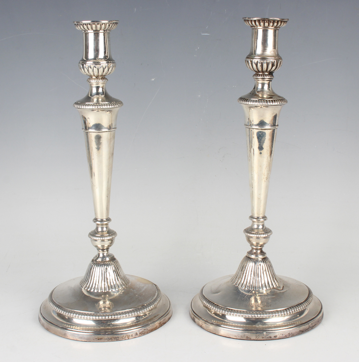 A pair of George III silver candlesticks, each sconce with reeded and foliate decoration above a