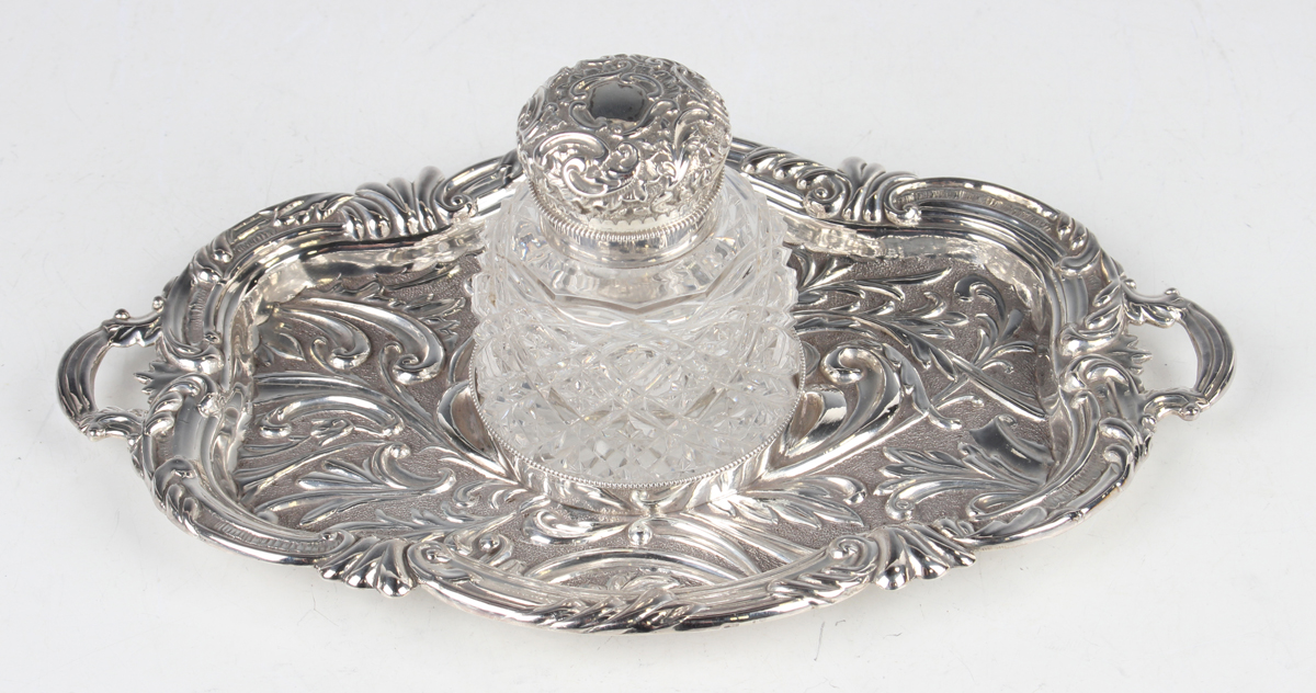 A late Victorian silver inkstand of shaped oval two-handled form, embossed with scrolling leaves