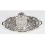 A late Victorian silver inkstand of shaped oval two-handled form, embossed with scrolling leaves