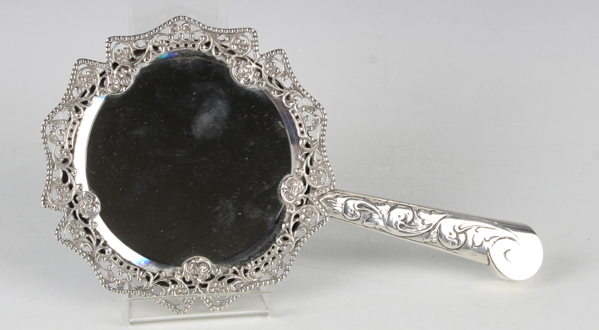 A Victorian silver mounted hand mirror with bevelled circular mirror plate within a cast and pierced