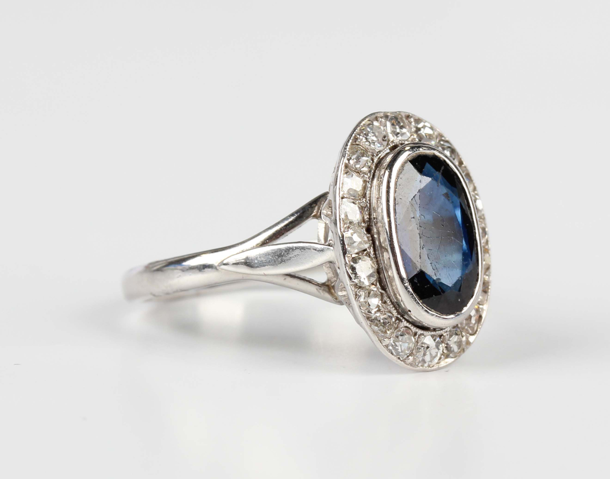 A white gold, sapphire and diamond oval cluster ring, collet set with an oval cut sapphire within