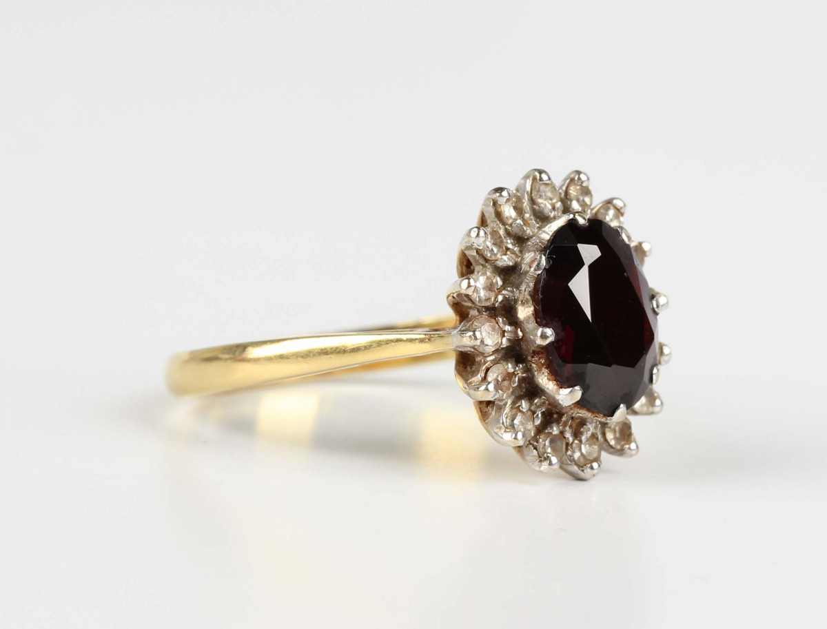 A gold, garnet and diamond cluster ring, claw set with an oval cut garnet within a surround of