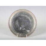 A George V silver circular card salver with raised bellflower and beaded rim, on claw and ball feet,