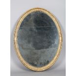 A George III giltwood oval wall mirror with a fluted and gadrooned frame, bordering a Vauxhall