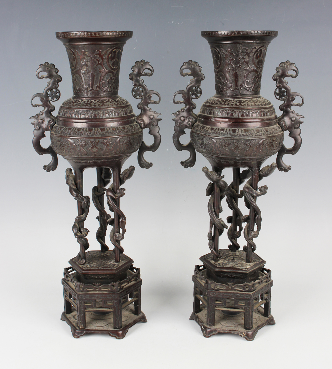 A pair of Japanese brown patinated bronze two-handled vases and integral stands, Meiji period,