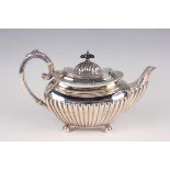An Edwardian silver half-reeded cushion shaped teapot with foliate capped scroll handle, on ball