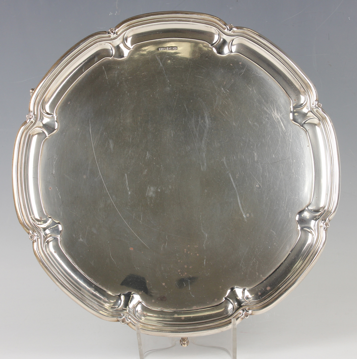 A George V silver circular salver with raised fleur-de-lis and lobed rim, on scroll legs,