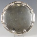 A George V silver circular salver with raised fleur-de-lis and lobed rim, on scroll legs,
