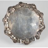 A George III silver card salver with raised scroll and scalloped rim, on three hoof feet, London
