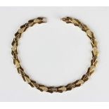 A gold bracelet in a pierced and stylized foliate link design with a partly textured finish, on a