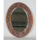 An early 20th century Arts and Crafts style walnut oval wall mirror, the frame carved with beasts