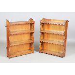 A very near pair of early 20th century Arts and Crafts oak four-tier wall shelves with shaped aprons