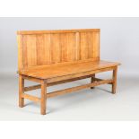 An early 20th century Arts and Crafts oak hall bench, the chamfered panel back and solid seat with