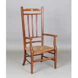 An Edwardian Arts and Crafts oak framed comb back elbow chair with a rush seat, height 109cm,