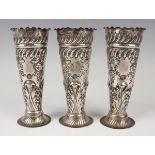 A set of three late Victorian silver vases, each of tapered cylindrical form, embossed with floral