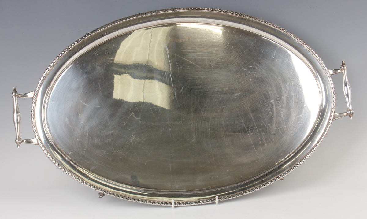 A George V silver oval tray with raised rim flanked by two scroll handles, on scroll legs, London