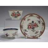 A Worcester teabowl and saucer, circa 1770, painted with famille rose flowers within an iron red and