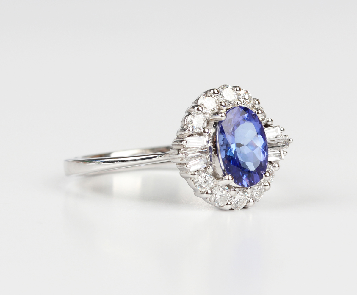 A white gold, tanzanite and diamond cluster ring, claw set with an oval cut tanzanite within a