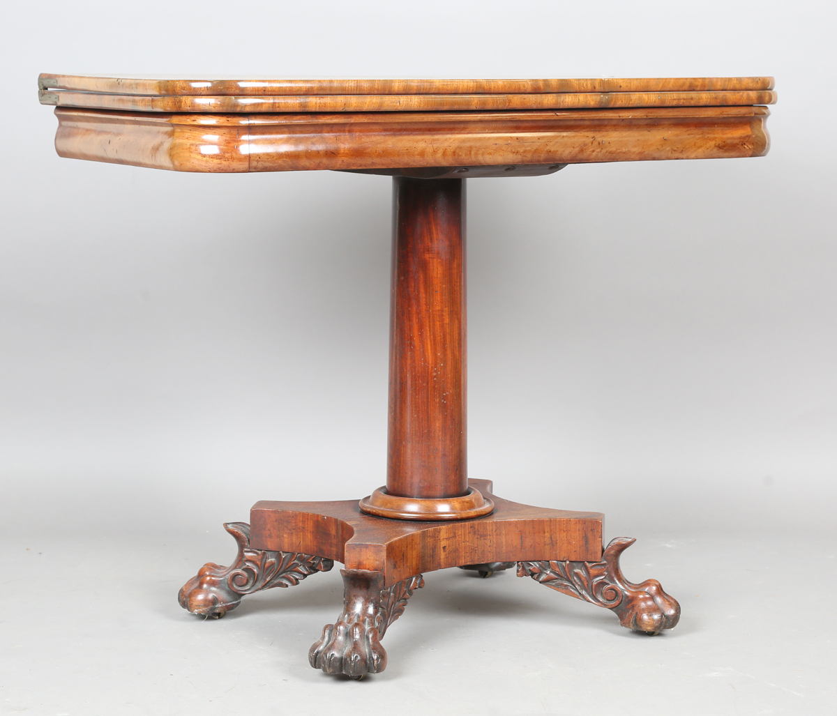 A George IV mahogany fold-over tea table, raised on a turned column and quatrefoil base, height