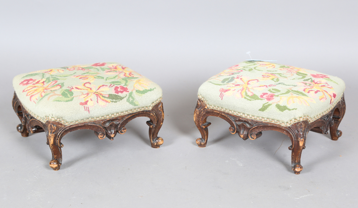 A pair of late Victorian walnut footstools, each with a needlework top, on carved legs, height 16cm,