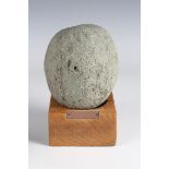 A medieval pale green stone cannon ball or trebuchet shot, length 15cm, mounted on a wooden plinth.