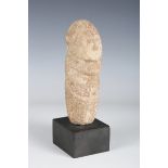 A carved stone votive burial figure, modelled with stylized facial and body features, raised on a