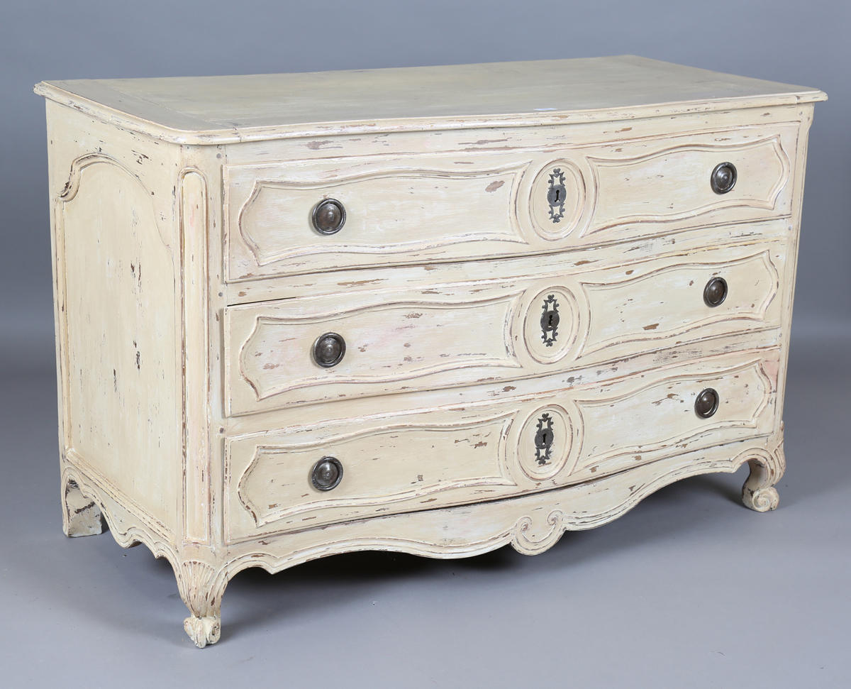 An 18th century French cream painted walnut serpentine fronted three-drawer commode, on carved squat