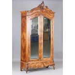 A late 19th century French walnut armoire with a carved pediment above a pair of mirrored doors