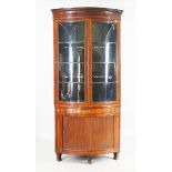 A late George III mahogany bowfront floor standing corner cabinet, the astragal glazed doors above