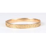 A 9ct gold oval hinged bangle with floral and scroll engraved decoration, Birmingham 1913, weight
